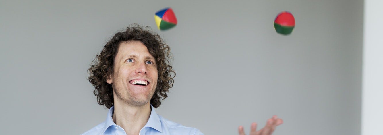 Lachender Geschäftsmann jongliert Bälle in seinem Büro